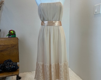 May include: A beige sleeveless dress with a satin sash and a lace trim. The dress is pleated and has a simple, elegant design.