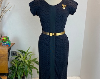 May include: A black vintage dress with a textured pattern, short sleeves, and a gold belt. The dress is on a mannequin.