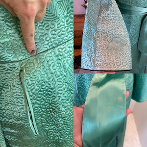 K&ouml;nnte beinhalten: Nahaufnahme einer vintage aqua-farbenen Steppjacke und eines passenden Sch&auml;rpenbands. Die Jacke hat aufwendige Stickmuster und ein dekoratives Emblem. Der Stoff weist einige Verf&auml;rbungen auf. Das Sch&auml;rpenband ist einfarbig aqua.