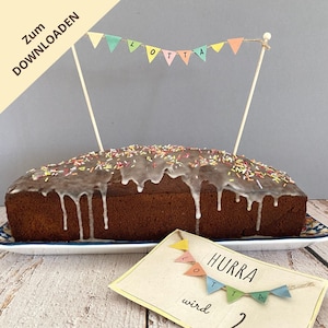 Può includere: Un dolce al cioccolato a forma di pane con glassa bianca e codette colorate. La torta è decorata con un bastoncino di legno con una fila di bandierine colorate che compongono la parola "LOTTA". Un biglietto con il testo "HURRA LOTTA wird" e una fila di bandierine colorate è in primo piano.