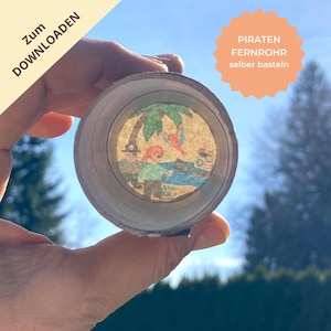 Może przedstawiać: Zrób to sam teleskop piracki trzymany na tle jasnoniebieskiego nieba. Teleskop wykonany jest z tekturowej tuby z okrągłym obrazem sceny pirackiej widocznym wewnątrz. Tekst na zdjęciu mówi "Zum Downloaden" i "PIRATEN FERNROHR selber basteln".