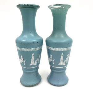 May include: Two blue ceramic vases with white Greek key designs and white figures in relief. The vases have a flared top and a round base.