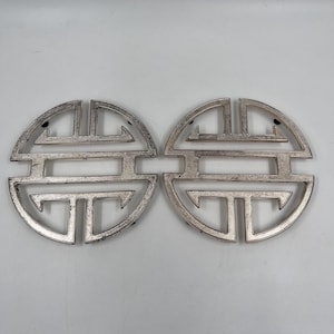 May include: Two silver-colored, decorative metal pieces. Each piece is a circular shape with an intricate, geometric design. The design features a series of connected shapes and lines, creating a symmetrical pattern. The pieces are likely used for home decor.