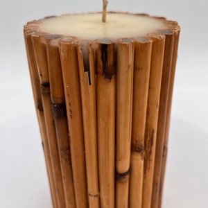 May include: A cylindrical candle with a beige wax top and a brown bamboo base. The candle is surrounded by a ring of brown bamboo sticks.