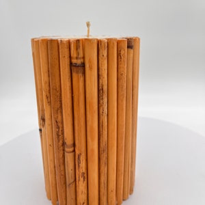 May include: A cylindrical candle made of natural bamboo sticks. The candle is a light brown color and has a single wick.
