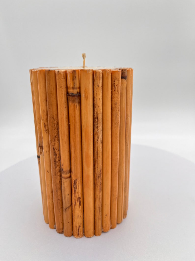 May include: A cylindrical candle made of natural bamboo sticks. The candle is a light brown color and has a single wick.