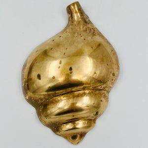 May include: A golden-colored, seashell-shaped decorative object. The shell has a spiral design and a textured surface with small dark spots. The top of the shell has a curved, horn-like shape.