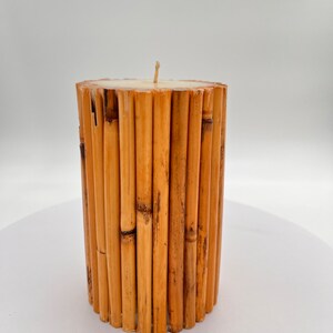 May include: A cylindrical candle made of natural bamboo sticks. The candle is white and has a single wick.