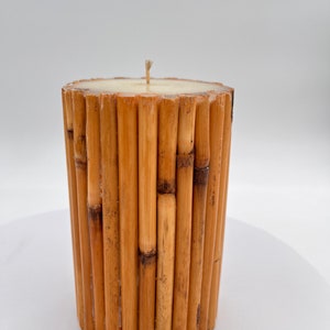May include: A cylindrical candle made of natural bamboo sticks. The candle is white and has a single wick.