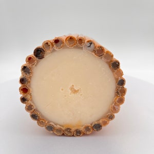 May include: A round, beige soap bar with a textured, brown bamboo-like outer layer. The soap is surrounded by a ring of small, round holes.