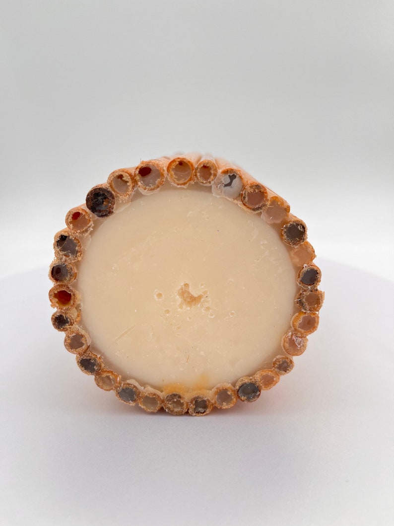 May include: A round, beige soap bar with a textured, brown bamboo-like outer layer. The soap is surrounded by a ring of small, round holes.