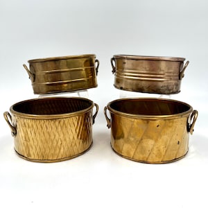 May include: Four small brass planters with handles. Two planters have a smooth finish, and two have a textured finish.