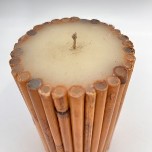 May include: A cylindrical candle with a beige wax top and a brown bamboo base. The candle has a single wick.