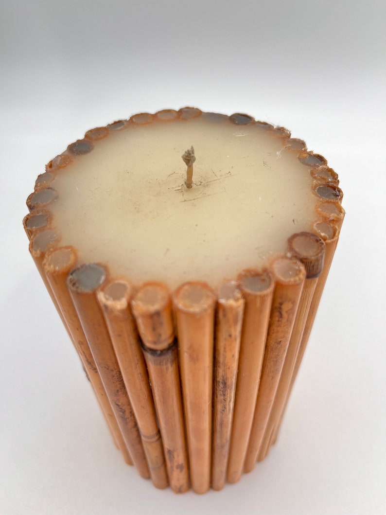 May include: A cylindrical candle with a beige wax top and a brown bamboo base. The candle has a single wick.