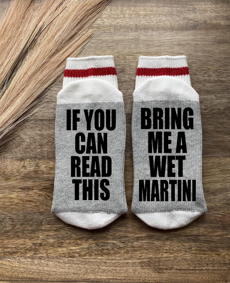 May include: A pair of gray socks with white and red stripes at the top. One sock says "If you can read this" and the other sock says "Bring me a wet martini".