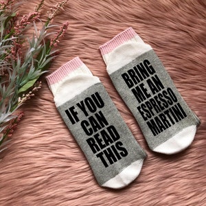 May include: A pair of gray and white socks with pink trim. One sock reads "If you can read this" and the other sock reads "Bring me an espresso martini".