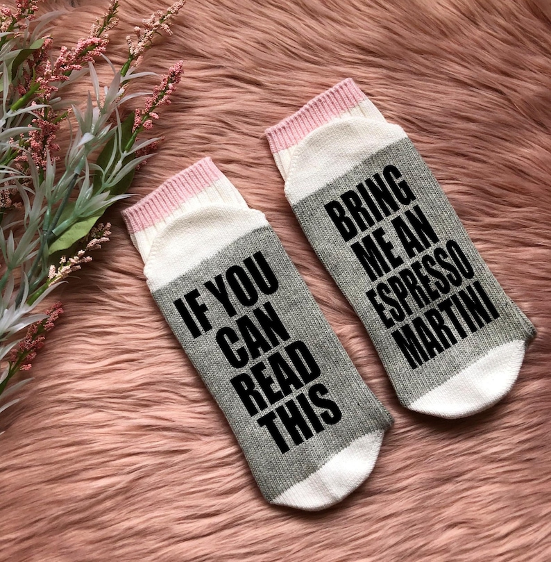 May include: A pair of gray and white socks with pink trim. One sock reads "If you can read this" and the other sock reads "Bring me an espresso martini".