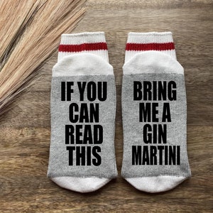 May include: A pair of gray socks with red and white stripes at the top. One sock says "If you can read this" and the other sock says "Bring me a gin martini".