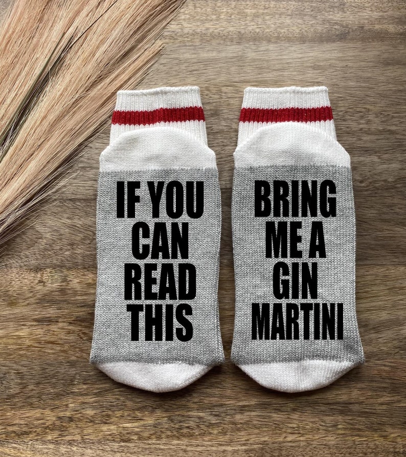 May include: A pair of gray socks with red and white stripes at the top. One sock says "If you can read this" and the other sock says "Bring me a gin martini".