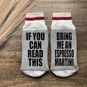 May include: A pair of gray socks with white and red stripes. One sock says "If you can read this" and the other sock says "Bring me an espresso martini".
