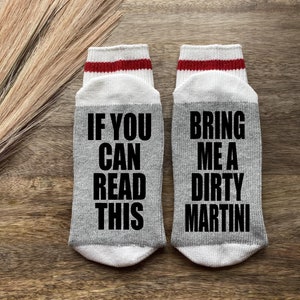 May include: A pair of gray socks with red and white stripes at the top. One sock says "If you can read this" and the other sock says "Bring me a dirty martini".