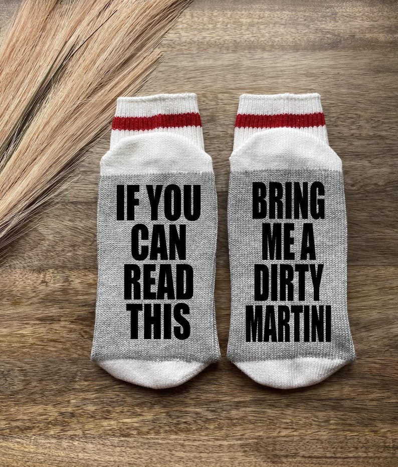 May include: A pair of gray socks with red and white stripes at the top. One sock says "If you can read this" and the other sock says "Bring me a dirty martini".