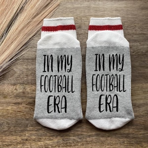 K&ouml;nnte beinhalten: Ein Paar graue Socken mit roten und wei&szlig;en Streifen oben. Die Socken haben den Text "In my football era" aufgedruckt.