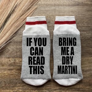 May include: A pair of gray socks with red stripes. One sock says "If you can read this" and the other sock says "Bring me a dry martini".