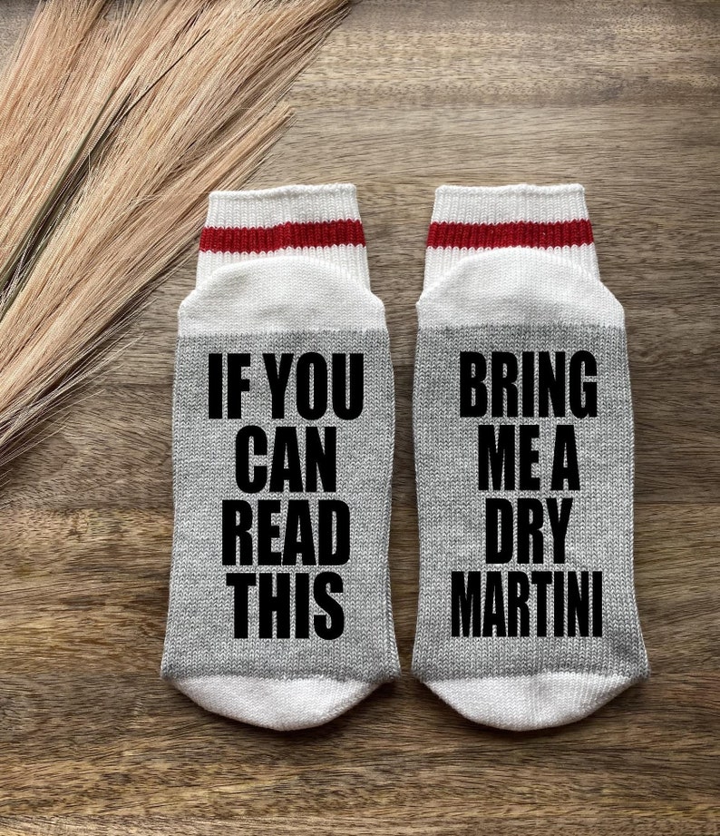May include: A pair of gray socks with red stripes. One sock says "If you can read this" and the other sock says "Bring me a dry martini".