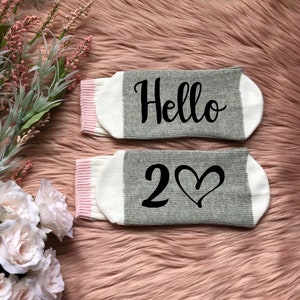 May include: A pair of gray and white socks with pink trim. One sock says "Hello" and the other says "2♡".