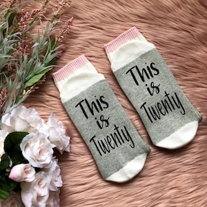May include: A pair of gray and white striped socks with pink trim. The socks have the text "This is Twenty" printed on them in black.