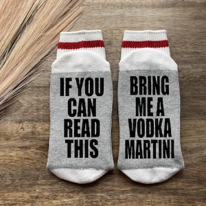 May include: A pair of gray socks with white and red stripes. One sock says "If you can read this" and the other sock says "Bring me a vodka martini".