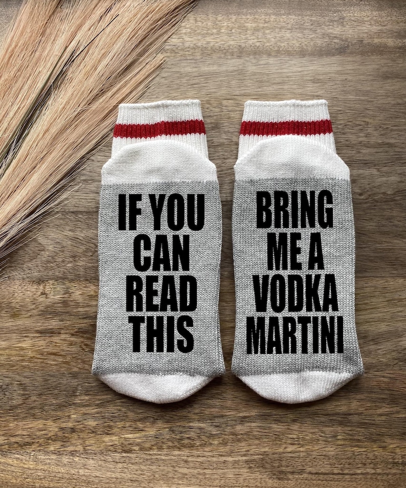 May include: A pair of gray socks with white and red stripes. One sock says "If you can read this" and the other sock says "Bring me a vodka martini".