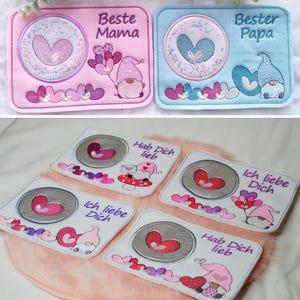 May include: Five embroidered patches with a heart and gnome design. The patches are white with pink, blue, and purple accents. The text on the patches reads "Beste Mama", "Bester Papa", "Hab Dich lieb", "Ich liebe Dich", and "Hab Dich lieb".