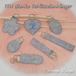 Pode incluir: Seis chaveiros de feltro diferentes com argolas de prata. Os chaveiros têm a forma de uma flor, um coração, um oval, um retângulo e dois retângulos de tamanhos diferentes. Todos os chaveiros são cinzentos com costuras cor-de-rosa. O texto "Dein Name" está bordado em um dos chaveiros. O texto "ITH Blank Schlüssellanhänger" está na parte superior da imagem.