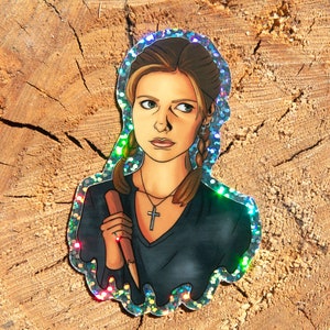 Buffy Summers from Buffy the Vampire Slayer glitter sticker. It is sitting on a piece of wood in the sun and the glitter is shining rainbow.