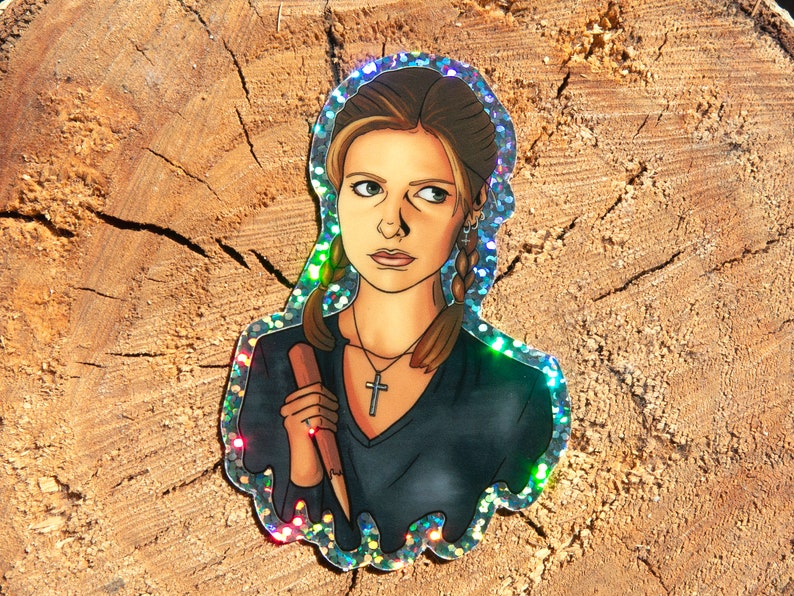 Buffy Summers from Buffy the Vampire Slayer glitter sticker. It is sitting on a piece of wood in the sun and the glitter is shining rainbow.