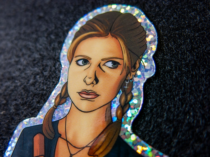 Close up of Buffy Summers sticker with glitter border and details. She is wearing a glittery cross and holding a wooden stake.