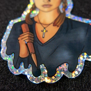 Close up of Buffy Summers sticker with glitter border and details. She is wearing a glittery cross and holding a wooden stake.