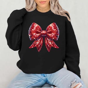 Puede incluir: Sudadera negra con un gran diseño de lazo rojo de lentejuelas.