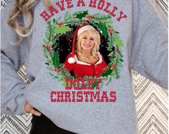 May include: Gray sweatshirt with a red and green holly wreath design featuring a photo of Dolly Parton wearing a Santa hat. The text "Have a Holly Dolly Christmas" is printed on the sweatshirt.