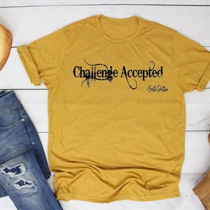 Könnte beinhalten: Ein senfgelbes T-Shirt mit dem Text "Challenge Accepted! - Beth Dutton" in Schwarz.