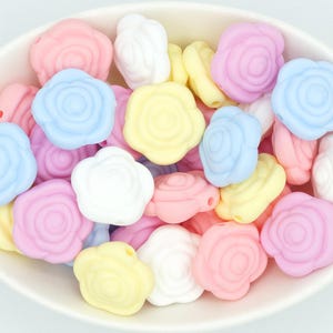 May include: A bowl filled with pastel-colored silicone rose-shaped beads. The beads are in shades of pink, blue, yellow, and white.
