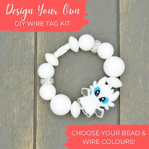 Puede incluir: Kit de etiquetas de alambre blanco DIY con cuentas blancas y un dije de dragón blanco. El kit dice "Design Your Own DIY Wire Tag Kit" sobre un fondo rojo. ¡Elige tus colores de cuentas y alambre!