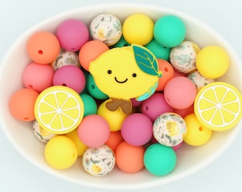 以下が含まれることがあります： ピンク、オレンジ、黄色、ティール色のカラフルなシリコンビーズが入った白いボウル。ボウルには、レモン型とレモンスライス型のシリコンチャームも含まれています。ビーズはマット仕上げです。