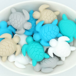 May include: A bowl filled with a variety of small silicone turtle toys in shades of blue, grey, and beige.