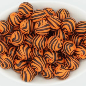 May include: A bowl filled with orange and black silicone beads with a tiger stripe pattern.