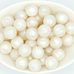 May include: A bowl filled with white silicone beads. The beads have a pearlescent finish and are smooth and round.