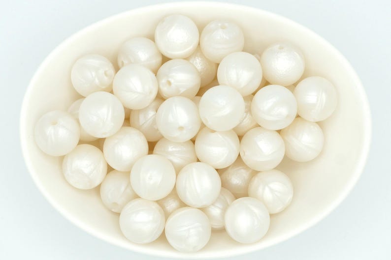 May include: A bowl filled with white silicone beads. The beads have a pearlescent finish and are smooth and round.