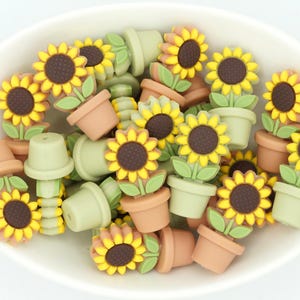 May include: A collection of small, colorful, plastic sunflower charms in green and brown pots. The charms are perfect for adding a touch of whimsy to crafts and jewelry.